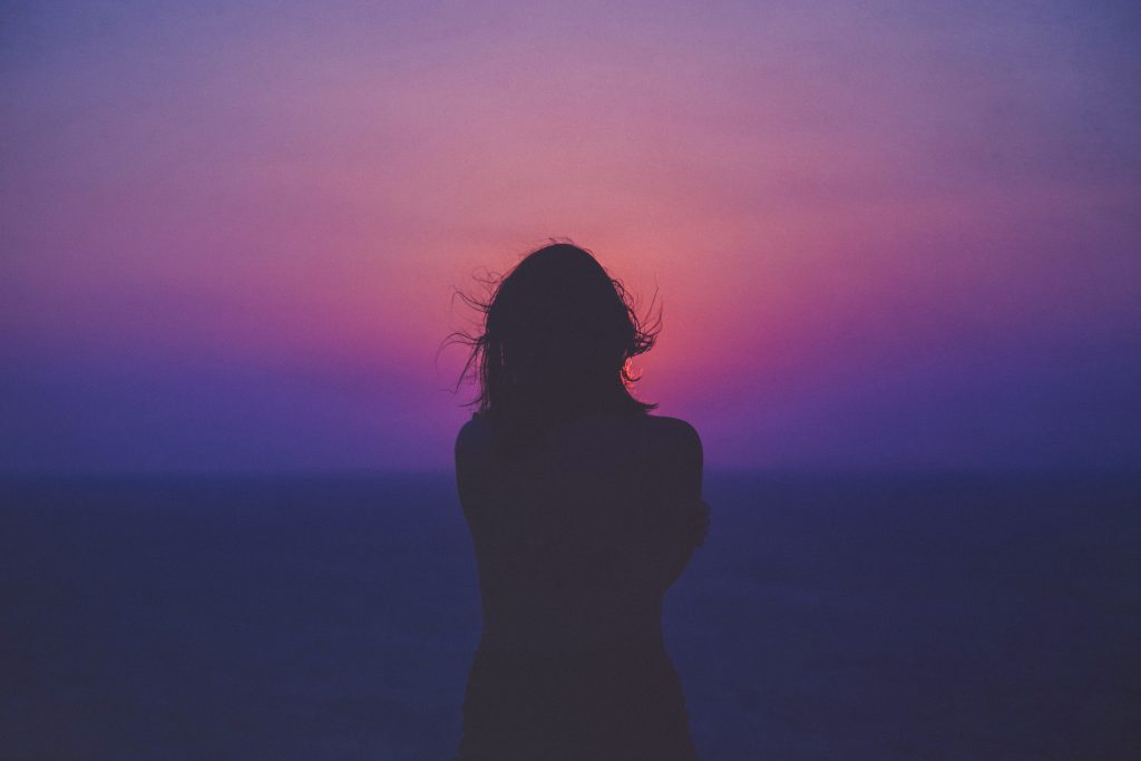 a woman looks out on a purple sunset