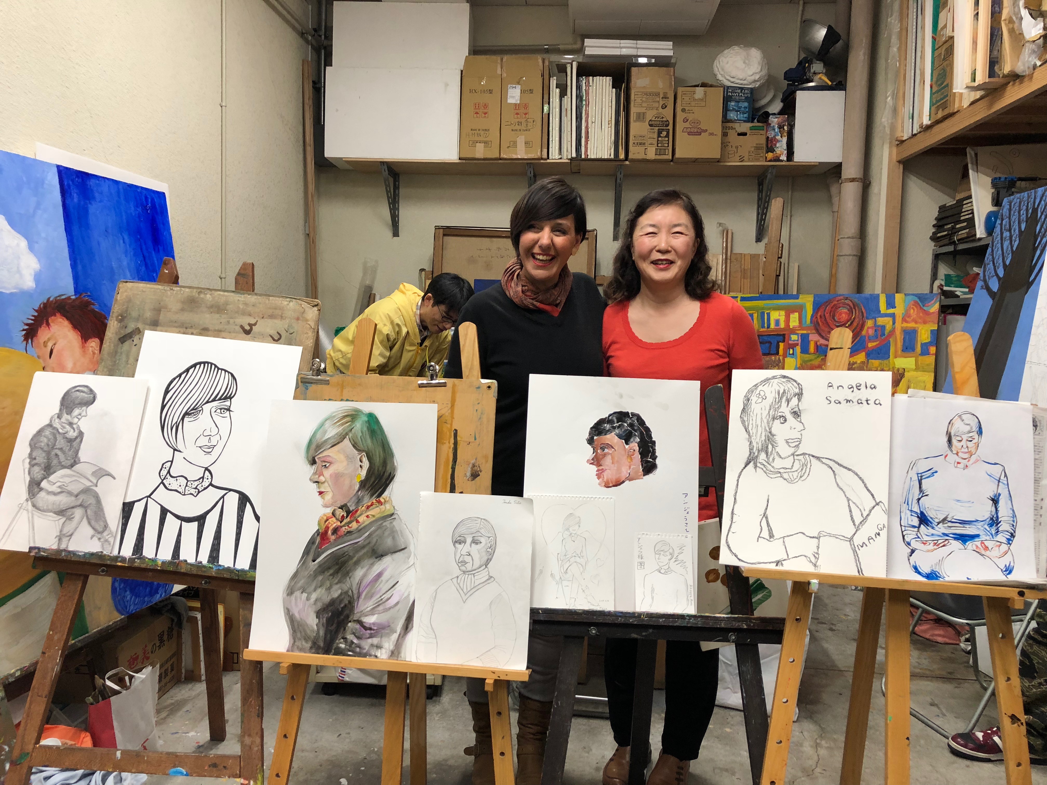 Two women are standing in an art workshop surrounded by easels and canvases. All the pictures and paintings are of Angela Samata who is on the left of the photo.